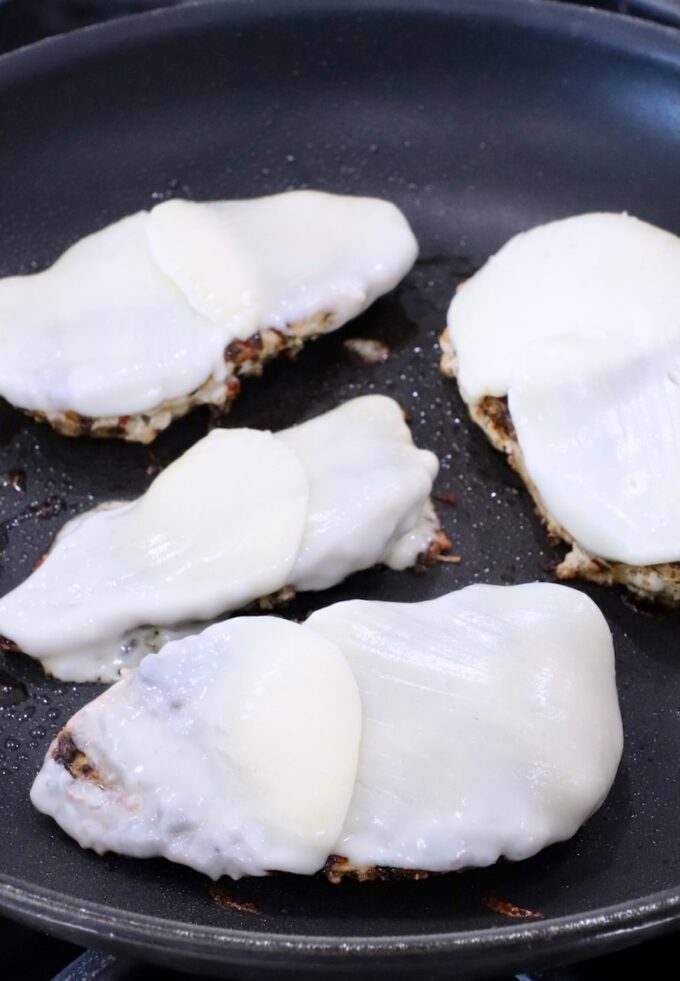 melted mozzarella cheese on top of chicken breasts in a skillet