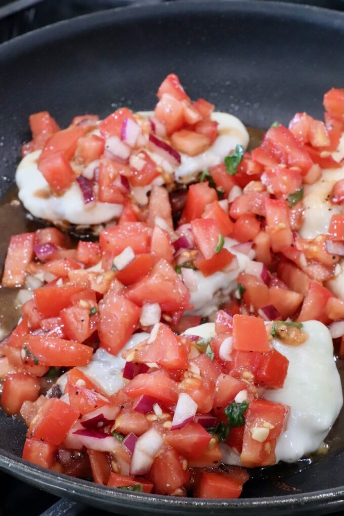 tomato bruschetta on top of chicken breasts in a skillet