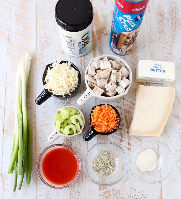 Ingredients for Buffalo Chicken Bake on a wooden surface divided in bowls and measuring cups. 