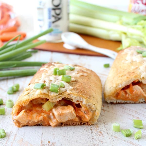 pizza dough stuffed with cubed buffalo chicken cut in half on a wooden surface.