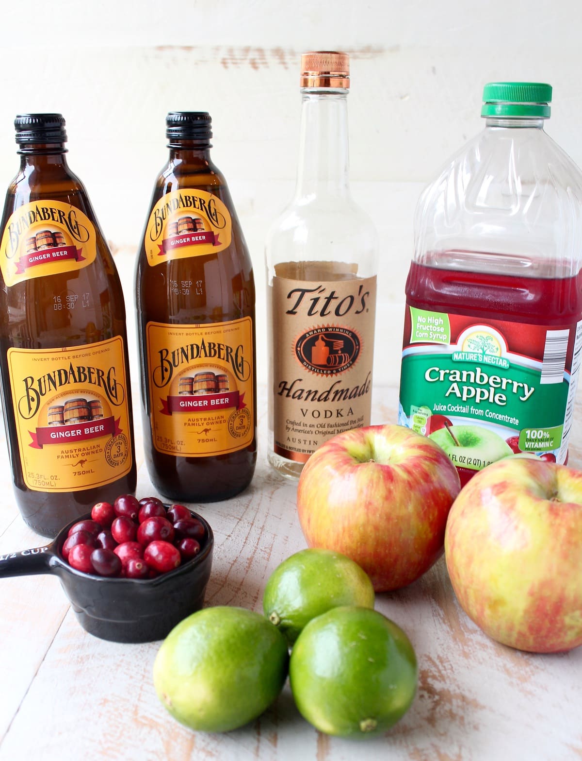 ingredients for cranberry apple moscow mule punch on a white wood board