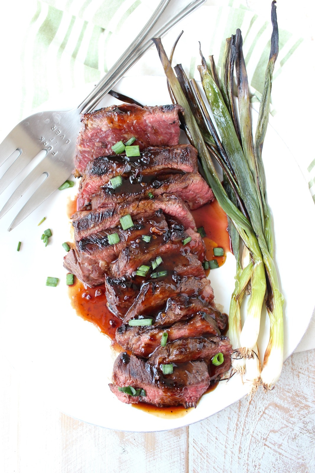 cooked sliced boneless short ribs on a plate with bbq sauce and grilled green onions