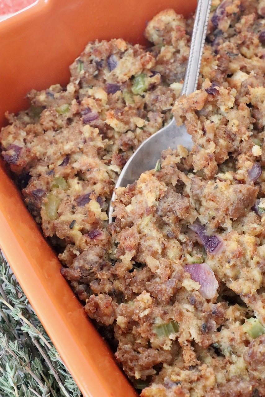 sausage stuffing in an orange baking dish with a serving spoon