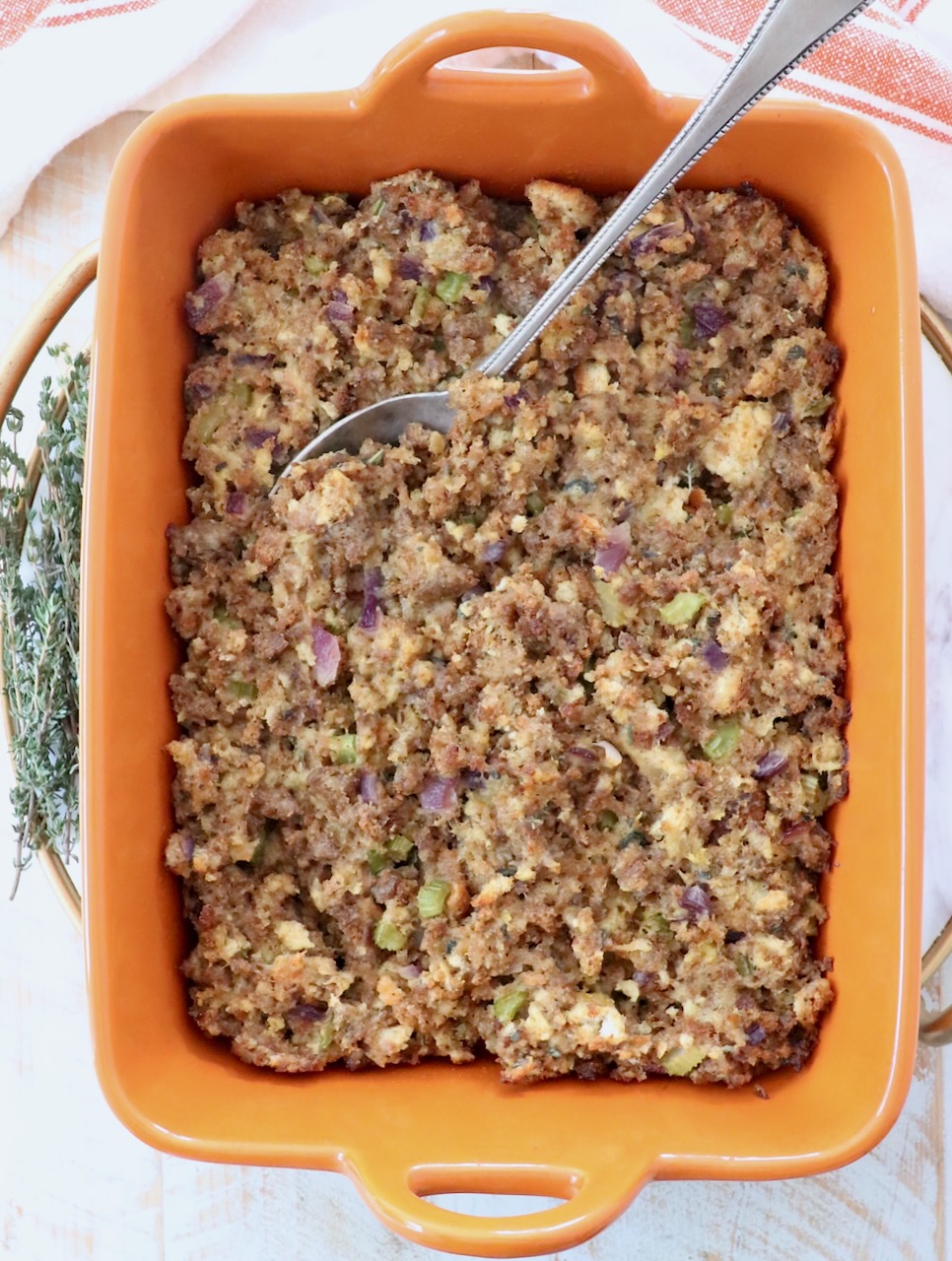 sausage stuffing in an orange casserole dish with a serving spoon