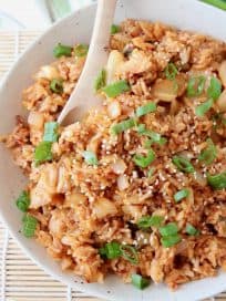Kimchi fried rice in bowl with spoon and topped with diced green onions