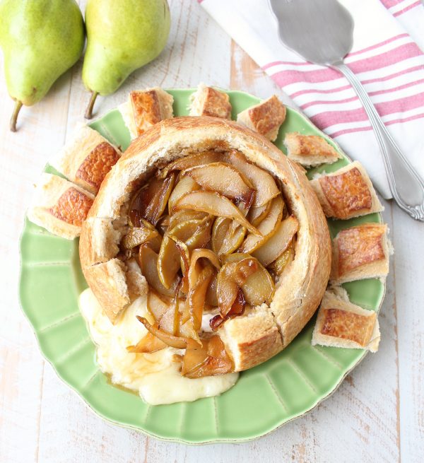 Caramelized pears on baked brie bread bowl on green plate with fresh pears