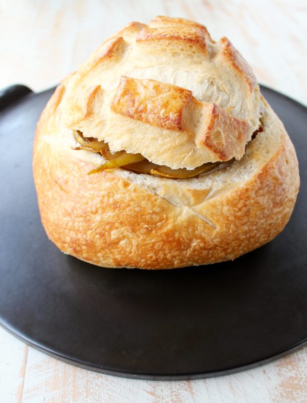 Sourdough bread bowl on baking sheet filled with brie and caramelized pears