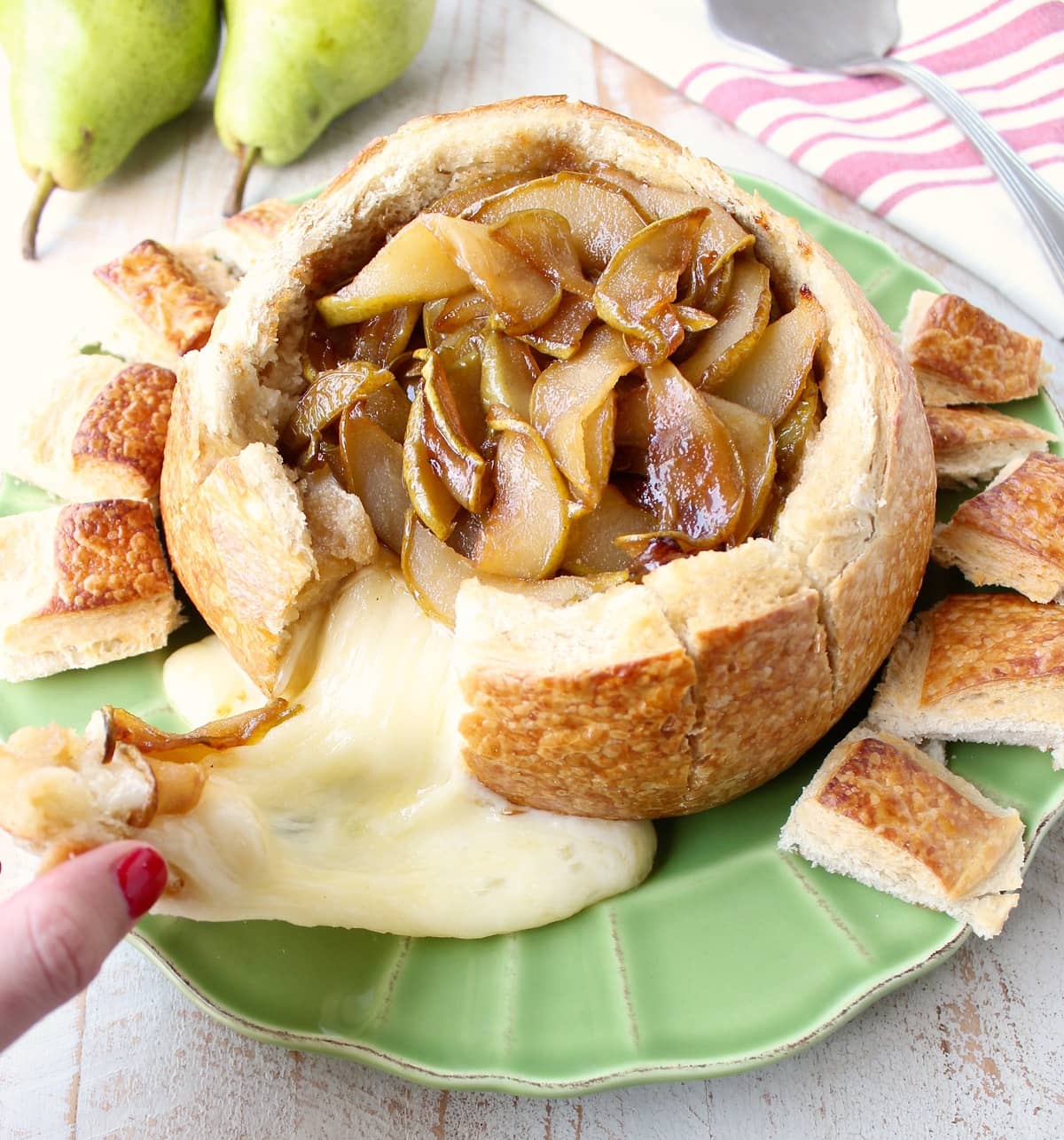 Brie cheese being pulled from a baked brie bread bowl with caramelized pears