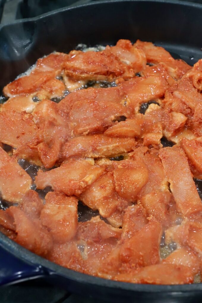 sliced raw chicken coated in spices, cooking in cast iron skillet
