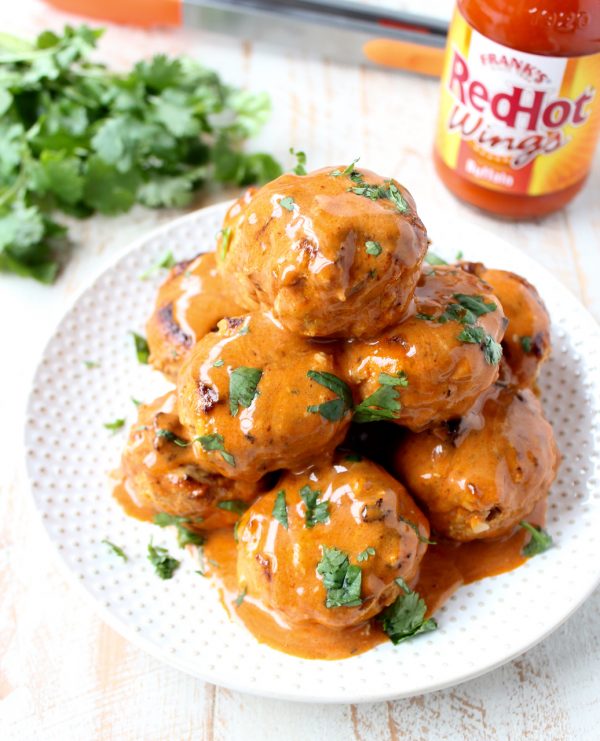 Meatballs covered in honey mustard and buffalo sauce on plate with fresh cilantro and bottle of buffalo sauce