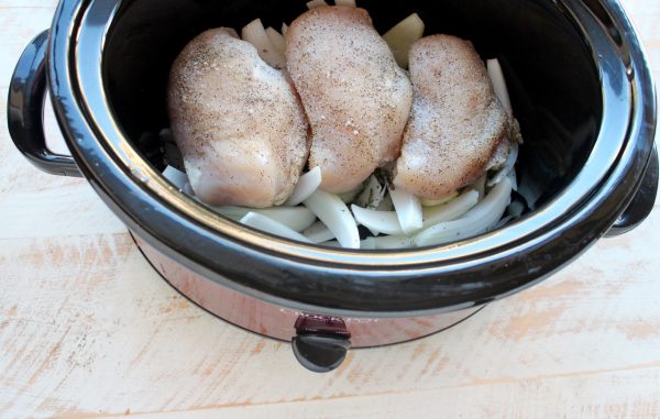 Seasoned chicken on top of sliced onions in a slow cooker.