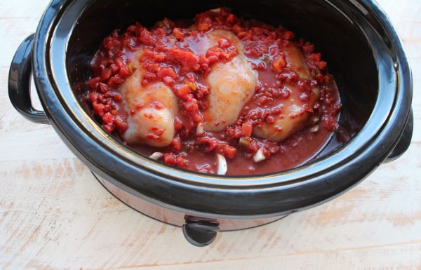 Raw chicken covered in red sauce in a slow cooker.