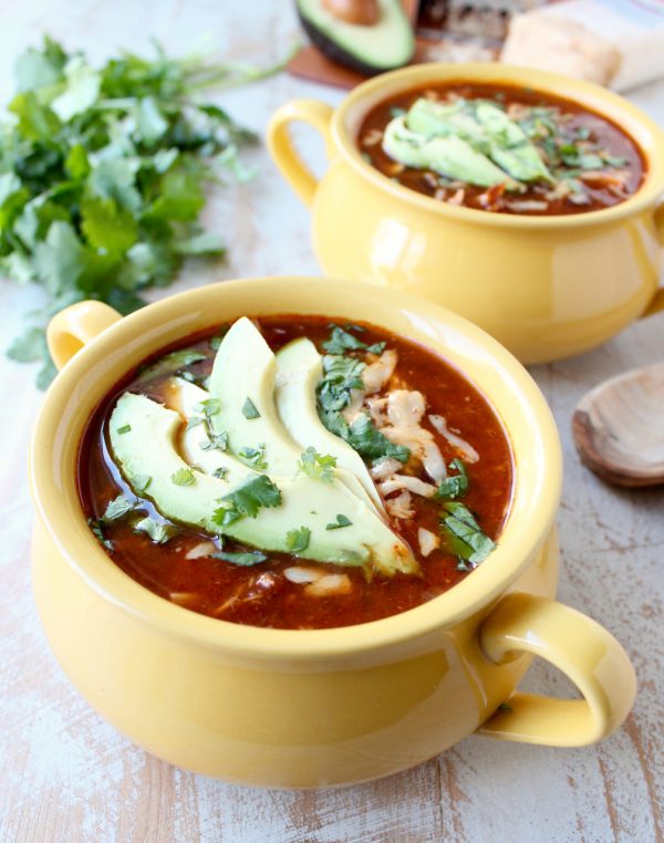 enchilada soup in yellow crock topped with sliced avocado