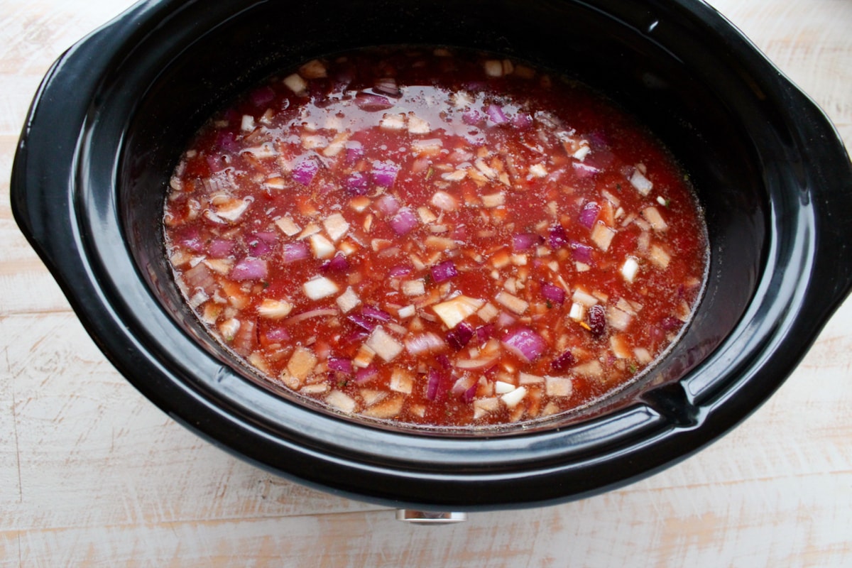 Slow Cooker filled with chicken broth, diced tomatoes with green chilies, sriracha, tomato paste, diced onions, corn, kidney beans and black beans.