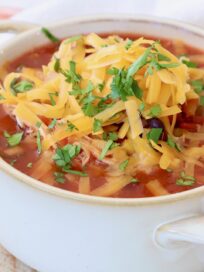 chicken enchilada soup in white crock topped with cheddar cheese