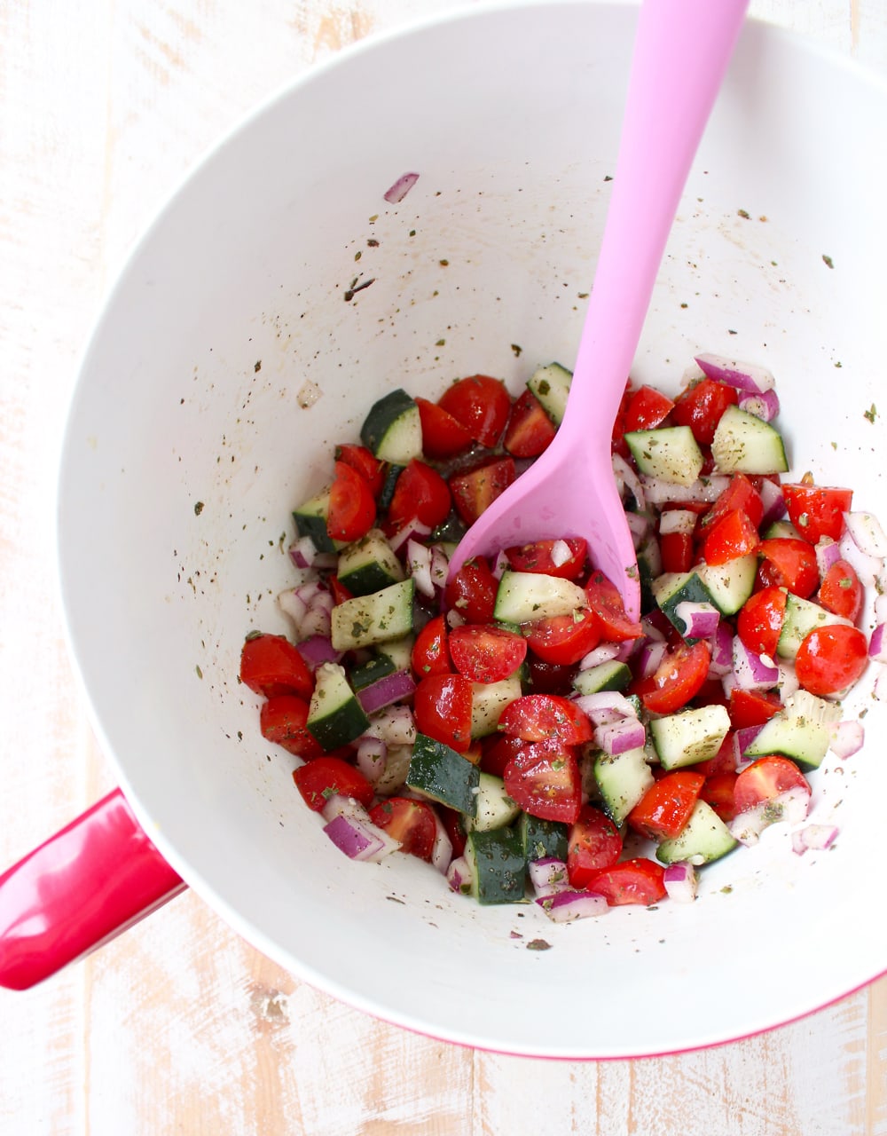 tomato cucumber salad in mixing bowl with pink spoon
