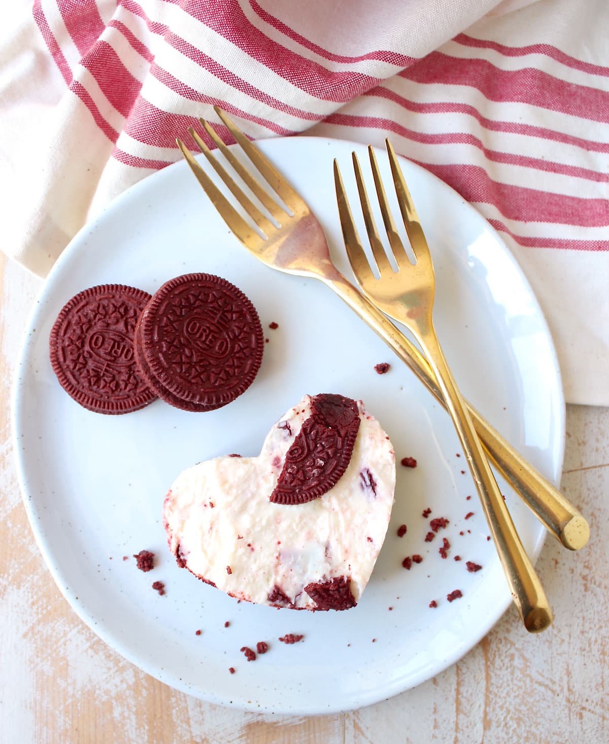 red velvet oreo cheesecake bar cut into a heart shape on a plate with gold forks