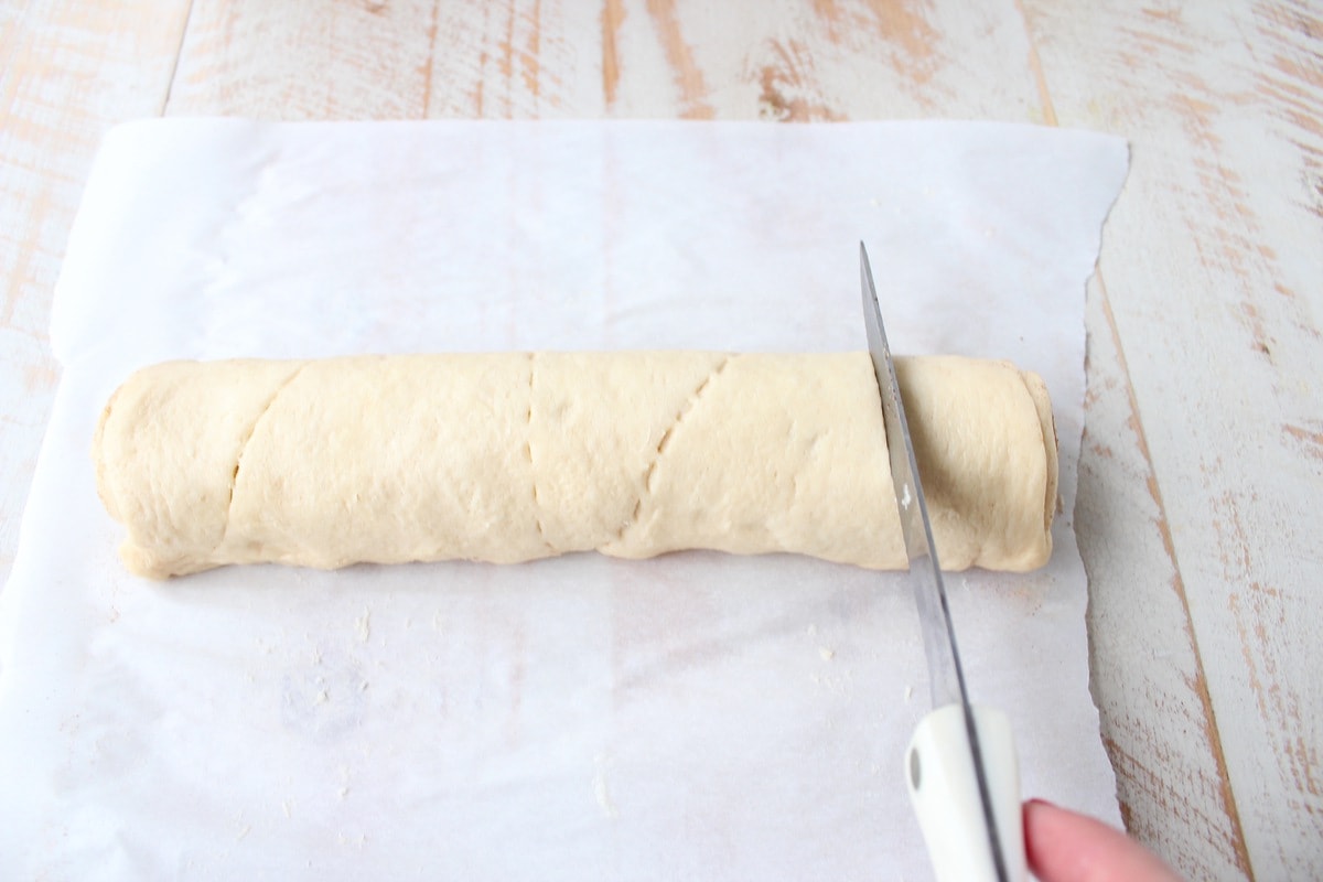 crescent dough roll being sliced with a knife on parchment paper