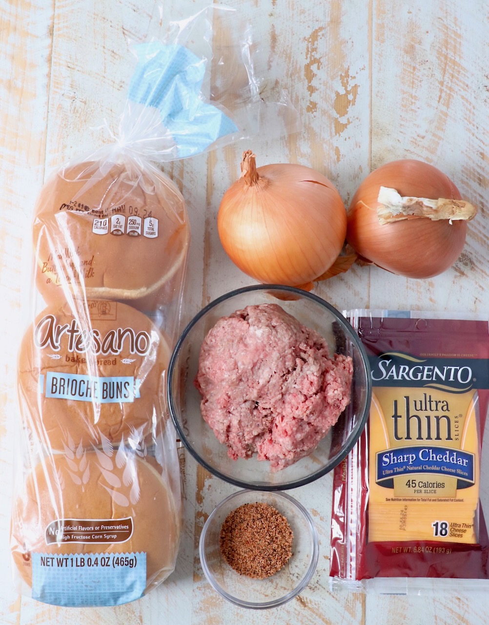 ingredients for onion fried burgers on white wood board
