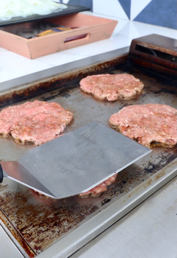 burger patties smashed with spatula on griddle