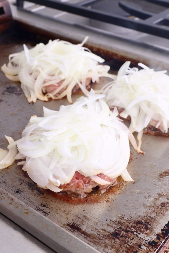 smashed burger patties on griddle topped with thinly sliced onions
