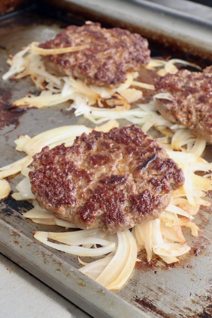 burger patties on top of grilled onions on griddle