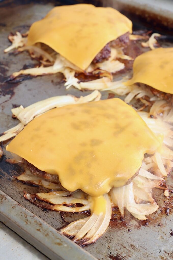 cheese topped fried onion burgers on griddle