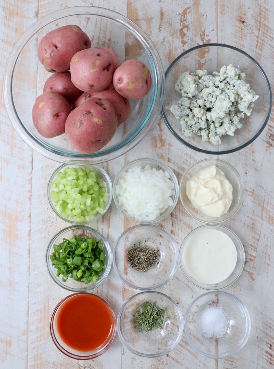 ingredients for buffalo potato salad in glass bowls on white wood board