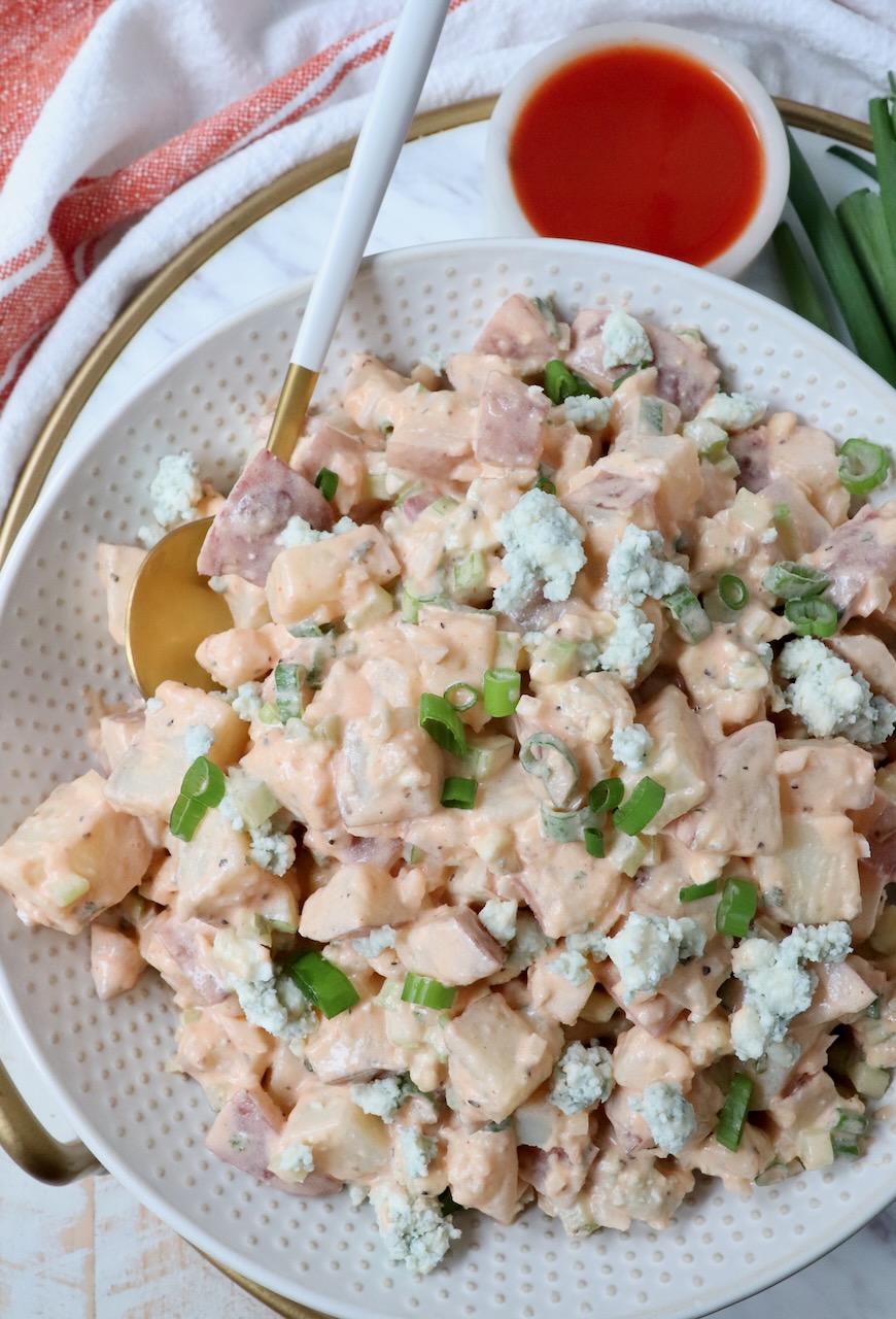 potato salad in bowl with spoon and small bowl of buffalo sauce on the side