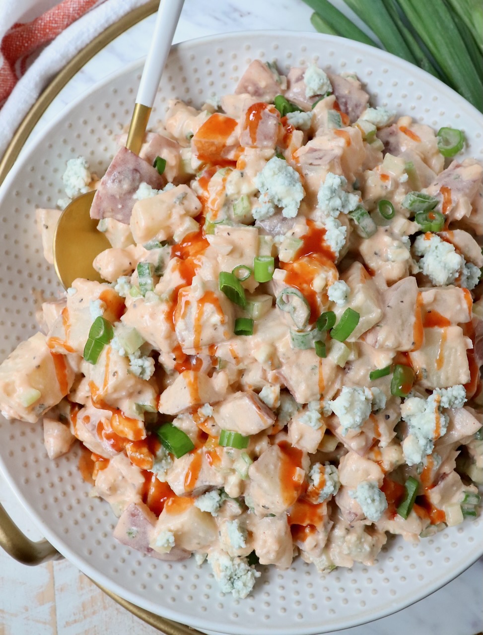 potato salad in bowl topped with a drizzle of buffalo sauce with a spoon in the bowl