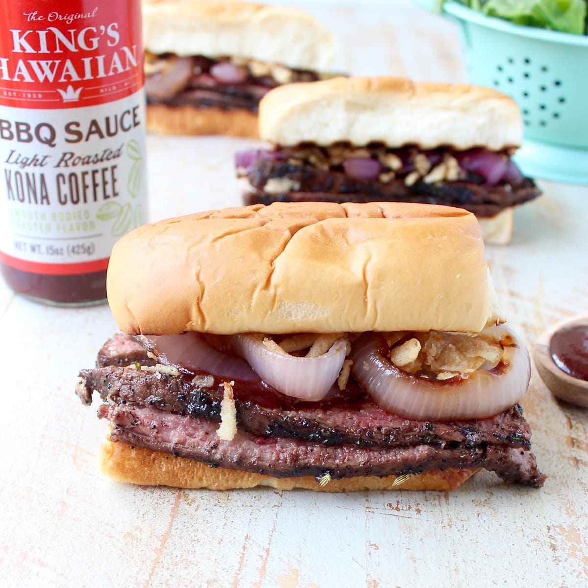 steak sandwiches on white wood board with bottle of bbq sauce in the background