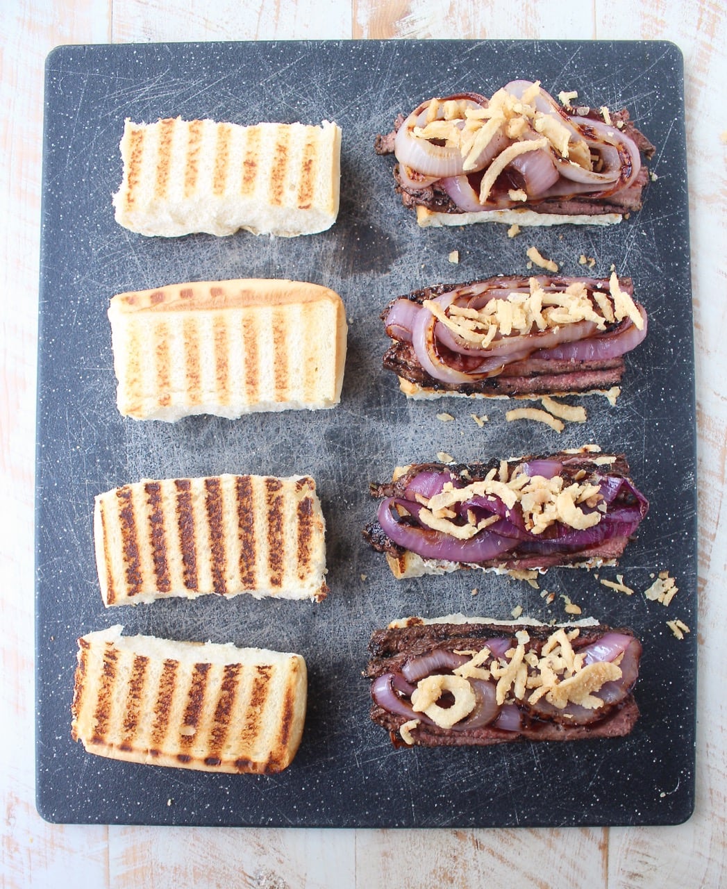 steak sandwiches on cutting board topped with grilled onions and crispy fried onions