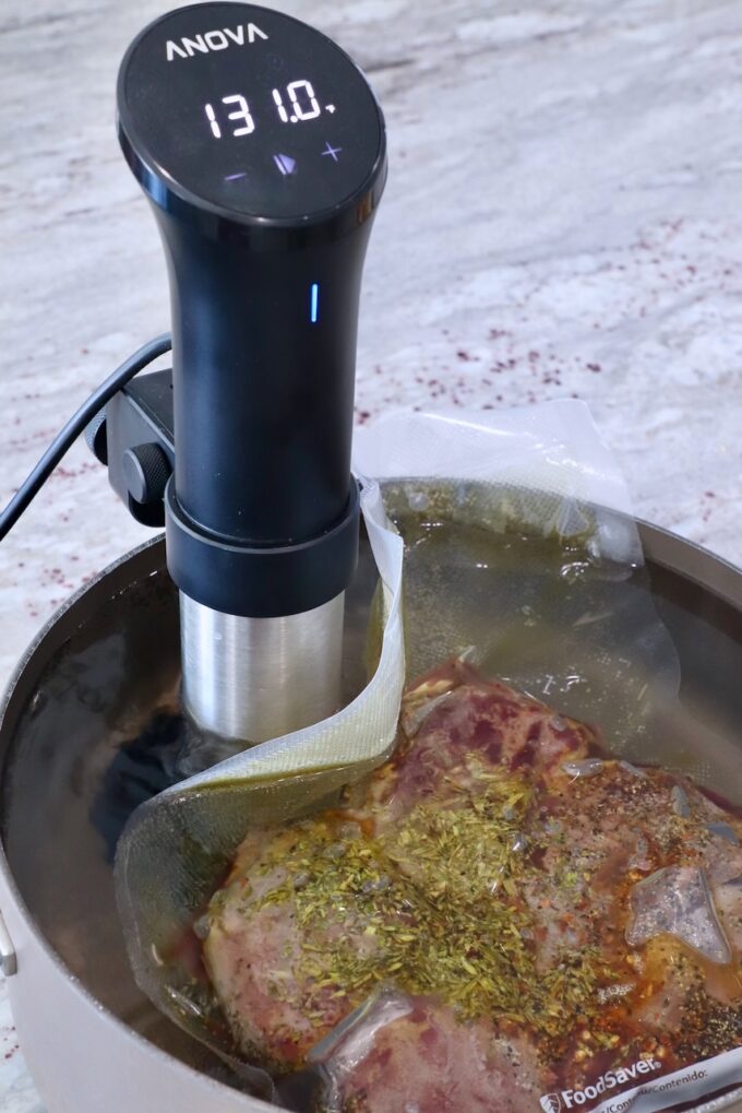 cooked steaks vacuum sealed in a bag in a large pot of water with a sous vide attached