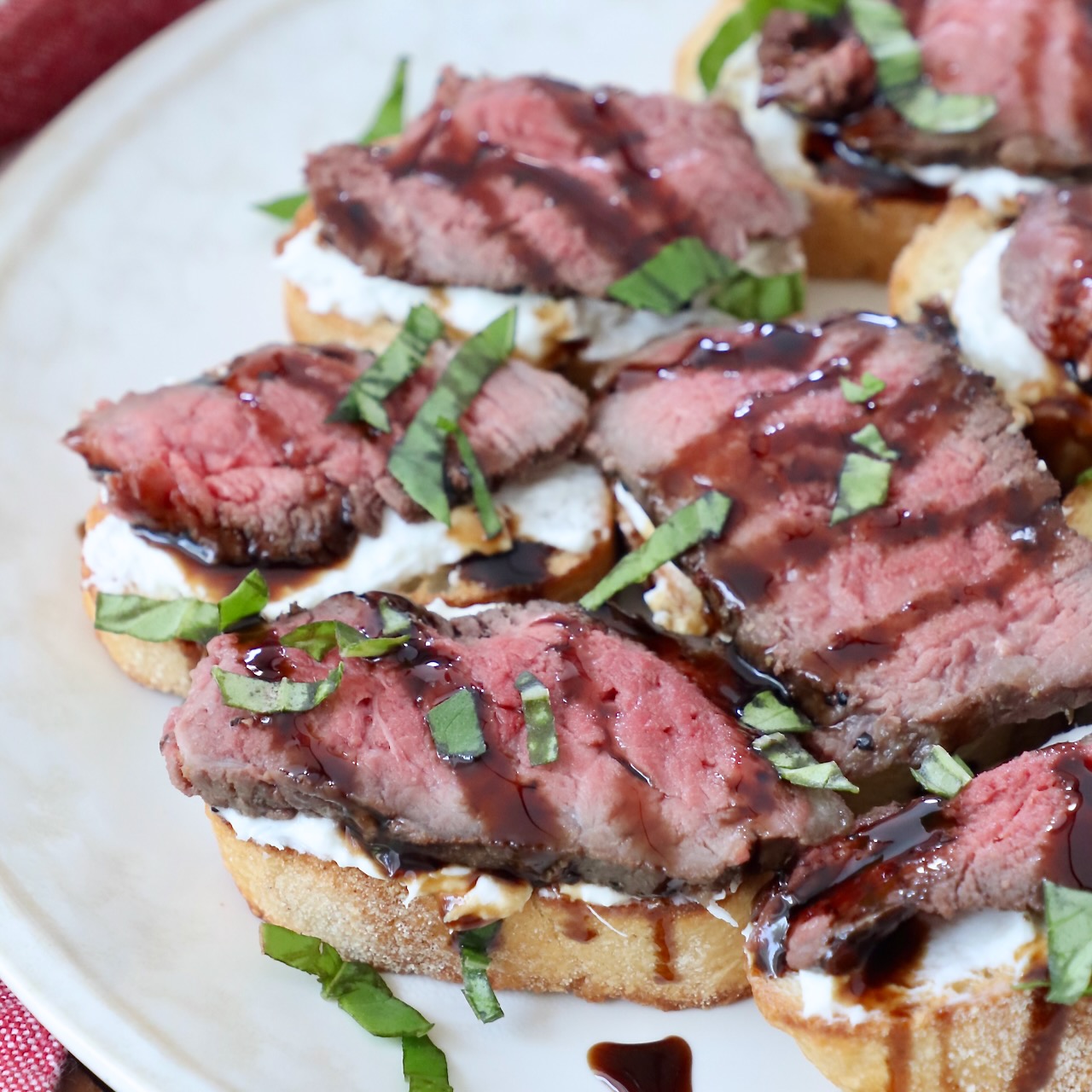 steak crostini on plate, topped with a drizzle of balsamic glaze