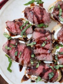 steak crostini on a plate topped with fresh chopped basil