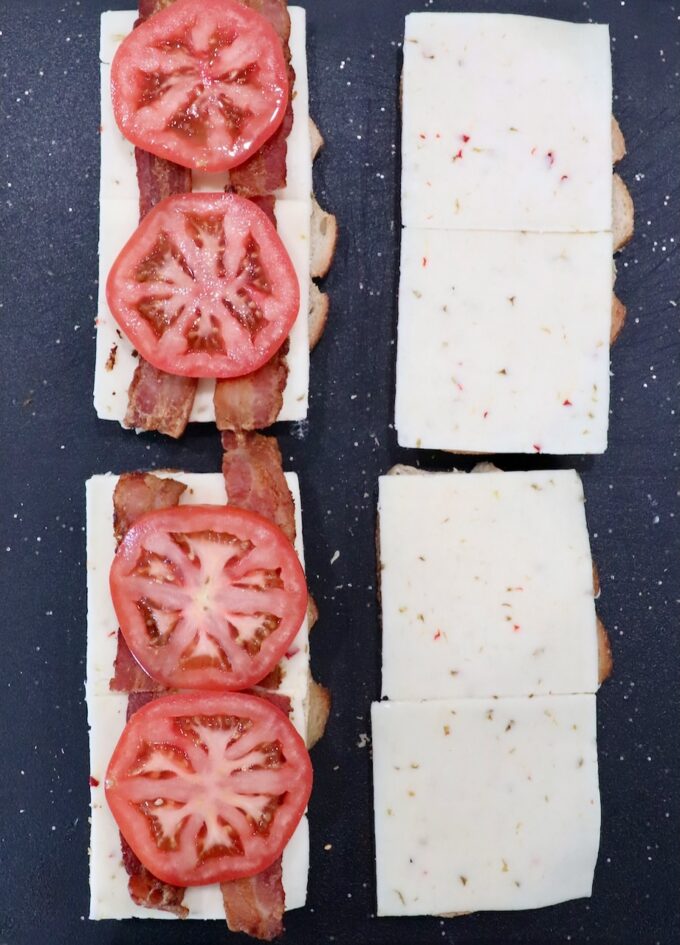 bread topped with slices of pepper jack cheese, bacon and sliced tomatoes on cutting board