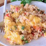 A plate of cheesy Mexican rice with ground meat, tomatoes, and cilantro, served on a white dish with a fork.
