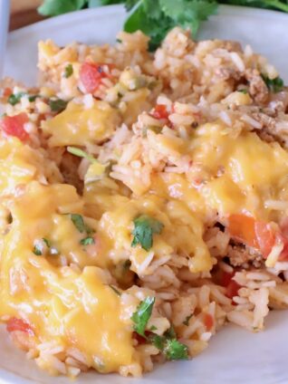 A plate of cheesy Mexican rice with ground meat, tomatoes, and cilantro, served on a white dish with a fork.