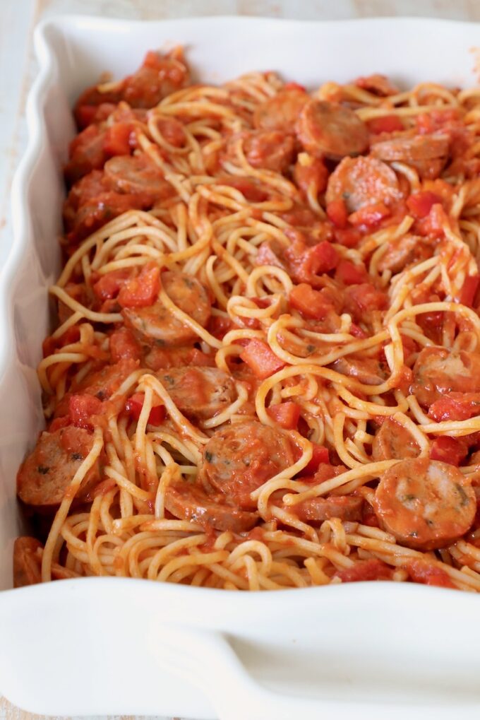 cooked spaghetti tossed with marinara sauce, sausage and peppers in casserole dish