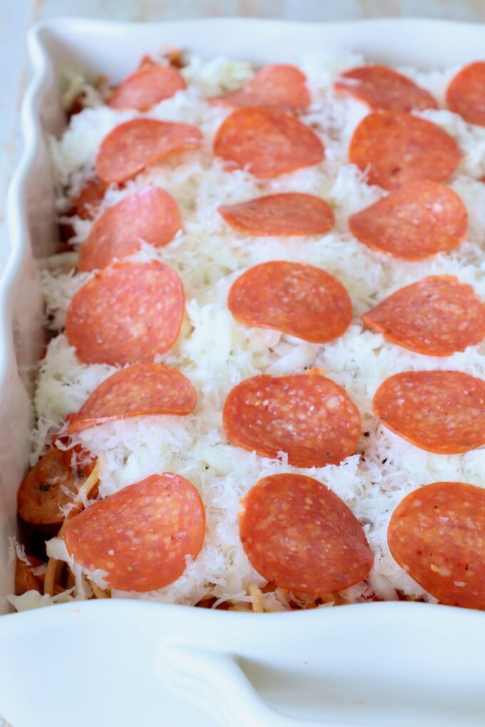 uncooked spaghetti casserole topped with shredded cheese and slices of pepperoni
