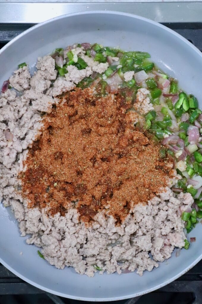 taco seasoning on top of cooked ground turkey and diced vegetables in a skillet