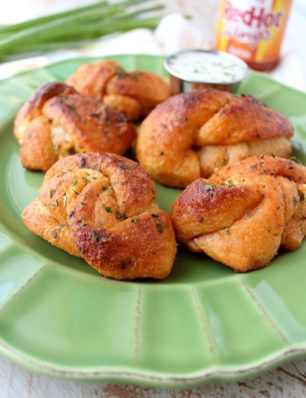 Mouth watering garlic knots are filled with cheese and smothered in buffalo sauce in this delicious recipe for cheesy garlic knots, perfect as an appetizer or party snack!