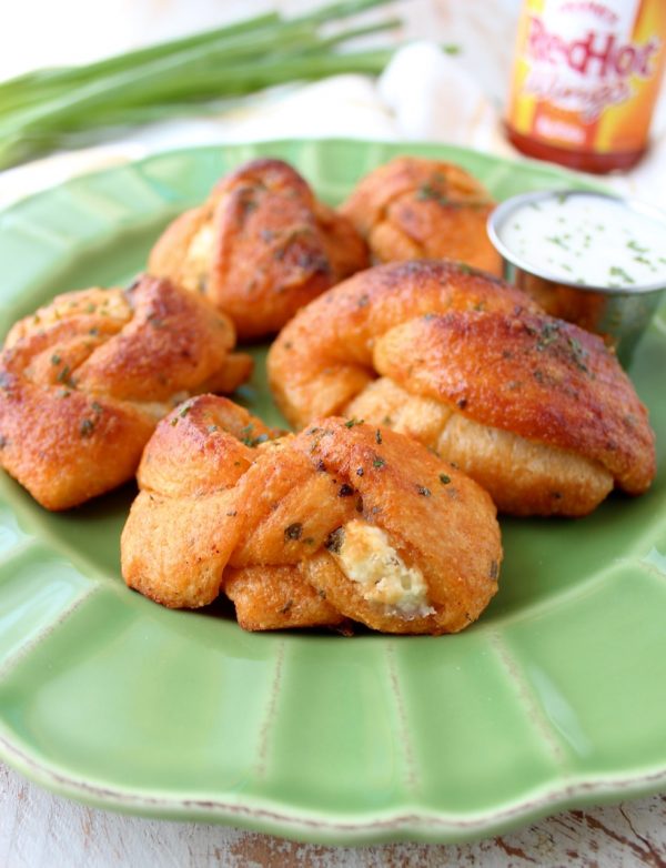 Mouth watering garlic knots are filled with cheese and smothered in buffalo sauce in this delicious recipe for cheesy garlic knots, perfect as an appetizer or party snack!