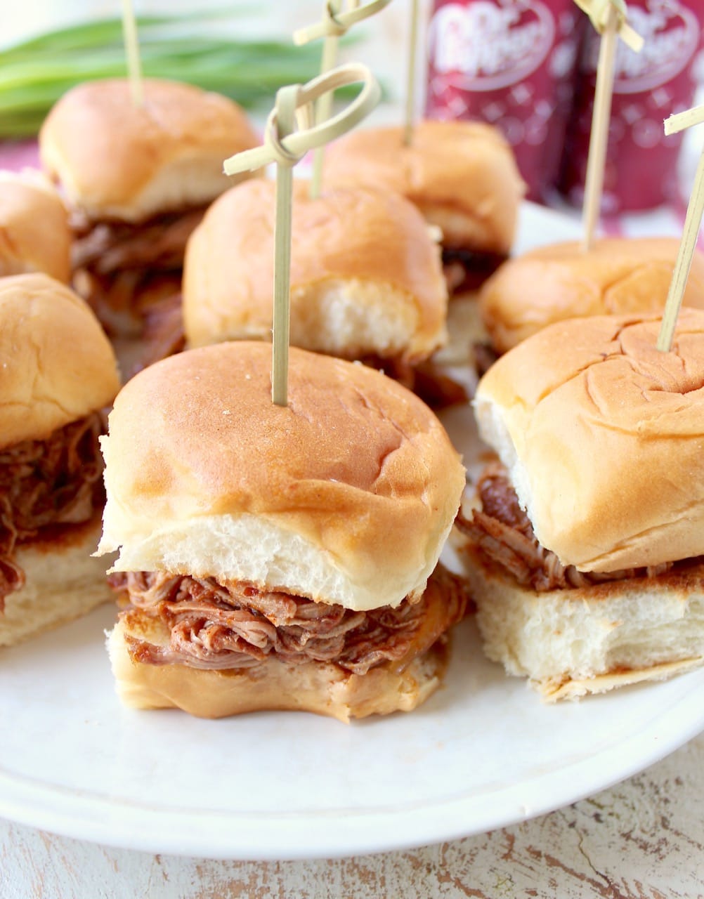 Mini pulled pork Hawaiian roll sandwiches on a white plate with a toothpick in each one. 