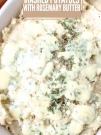 Close-up of creamy mashed potatoes topped with melted blue cheese and sprinkled with rosemary in a white dish.