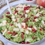 brussels sprout salad in a bowl topped with diced apples and pomegranate seeds