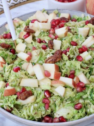 brussels sprout salad in a bowl topped with diced apples and pomegranate seeds