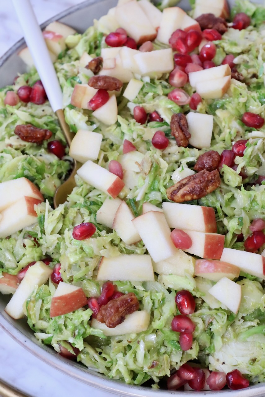 brussels sprout salad in a bowl topped with pomegranate seeds and apples