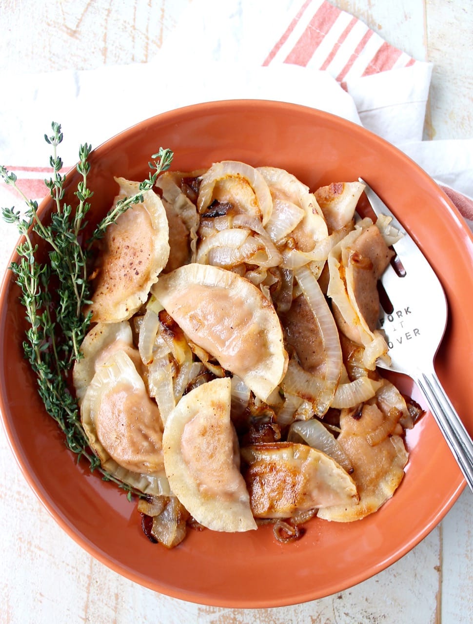 cooked pierogies and caramelized onions in an orange bowl with fresh thyme