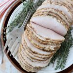 sliced turkey breast on a plate with fresh thyme and a serving fork